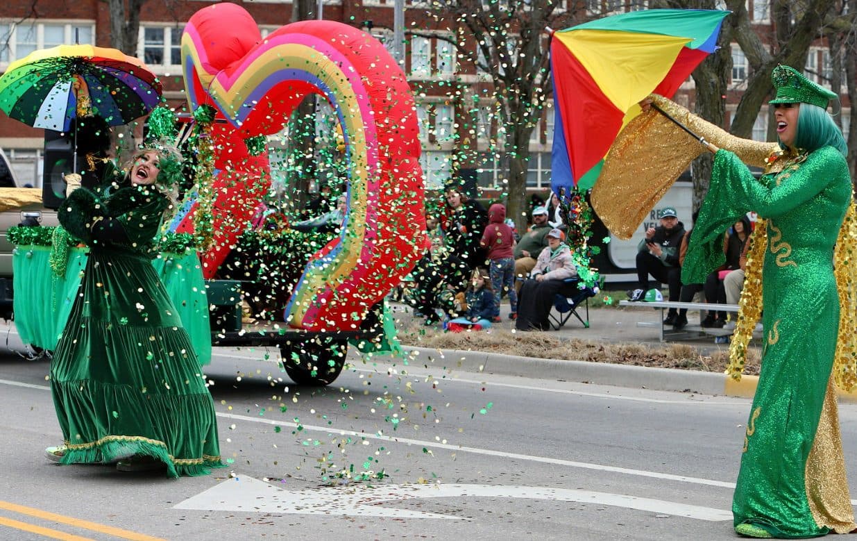 Performers in green gowns throwing confetti in front of a rainbow float